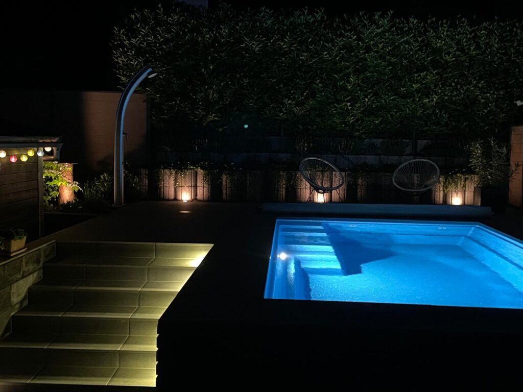 Beleuchteter Pool am Abend mit Treppenbereich.