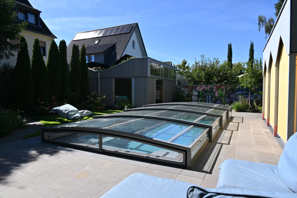 CompassPool als Überlaufpool mit flacher Glasüberdachung zwischen Wohnhaus und Gartenhaus