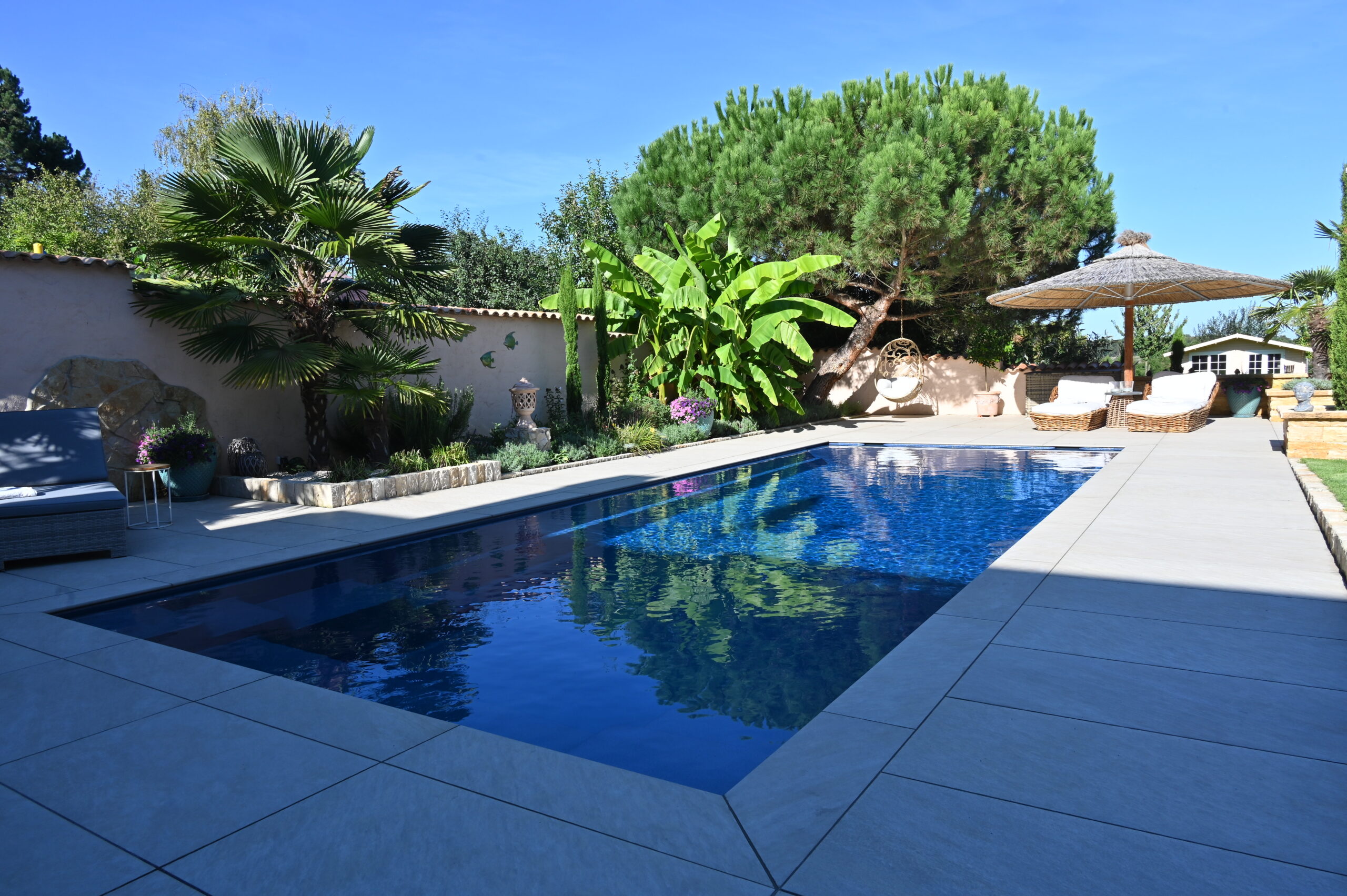 Pool mit heller Terrasse und mediterraner Bepflanzung