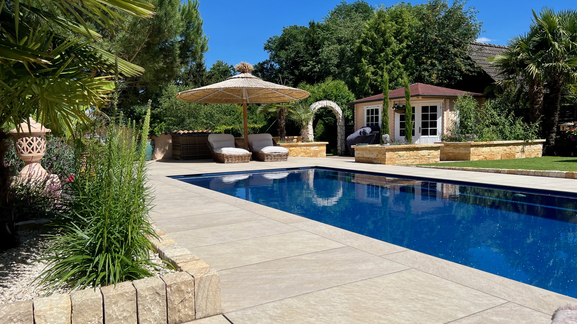 Moderner Pool mit heller Terrassenfläche und Poolhaus