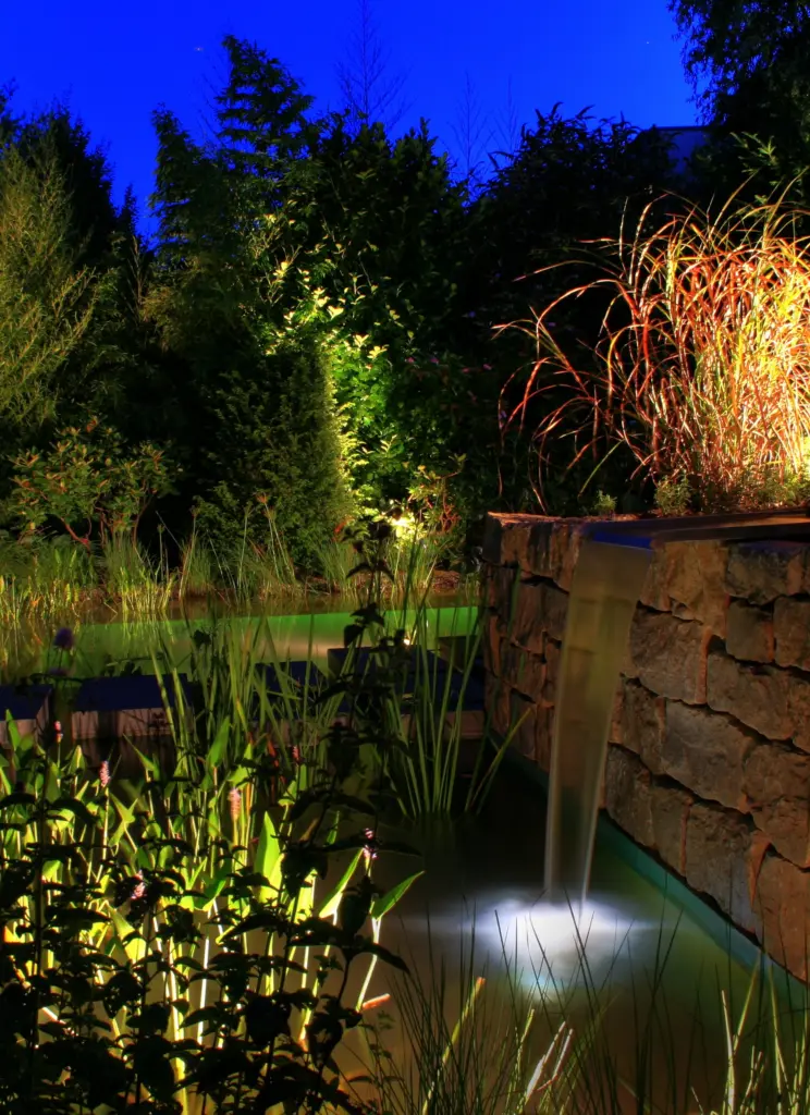 Schwimmteich mit Gartenbeleuchtung und bepflanztem Uferbereich