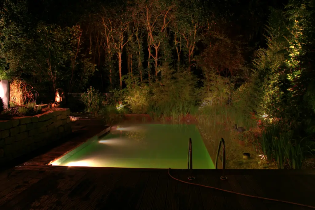 Beleuchtete Wasserfläche des Schwimmteichs im eingewachsenen Garten