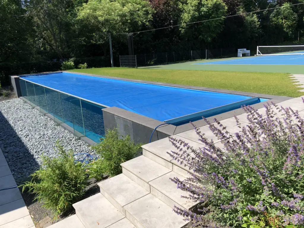 Geschlossene blaue Poolabdeckung auf dem Glaswandpool