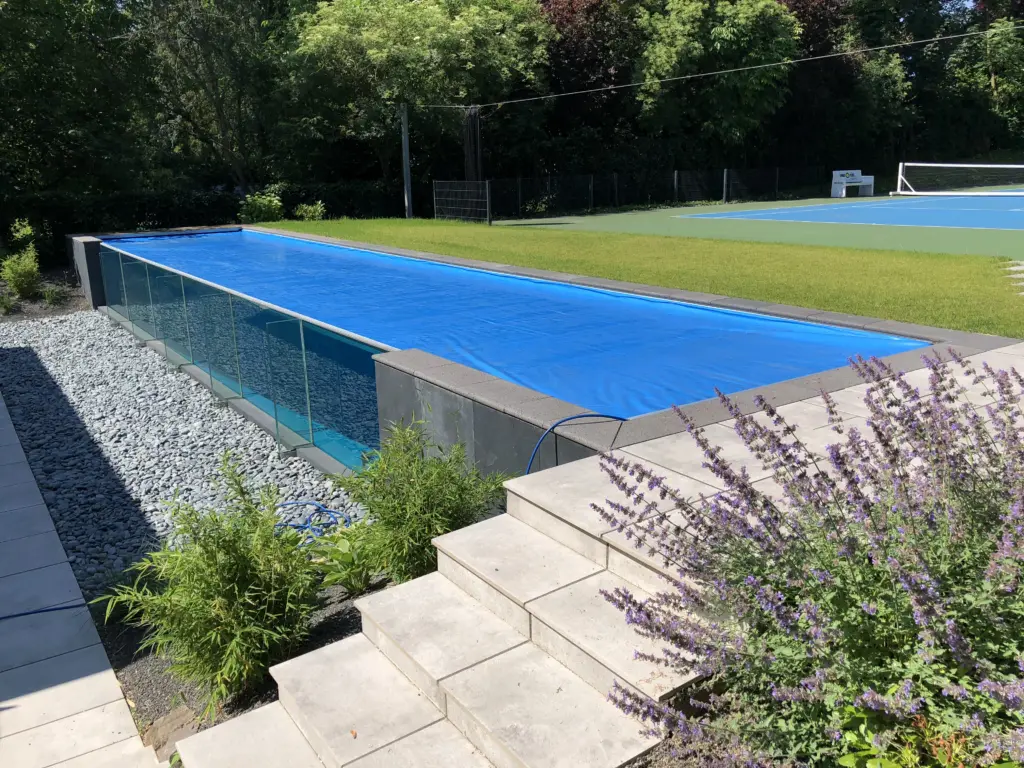 Glaswandpool mit Poolabdeckung, Stufen und bepflanztem Beet