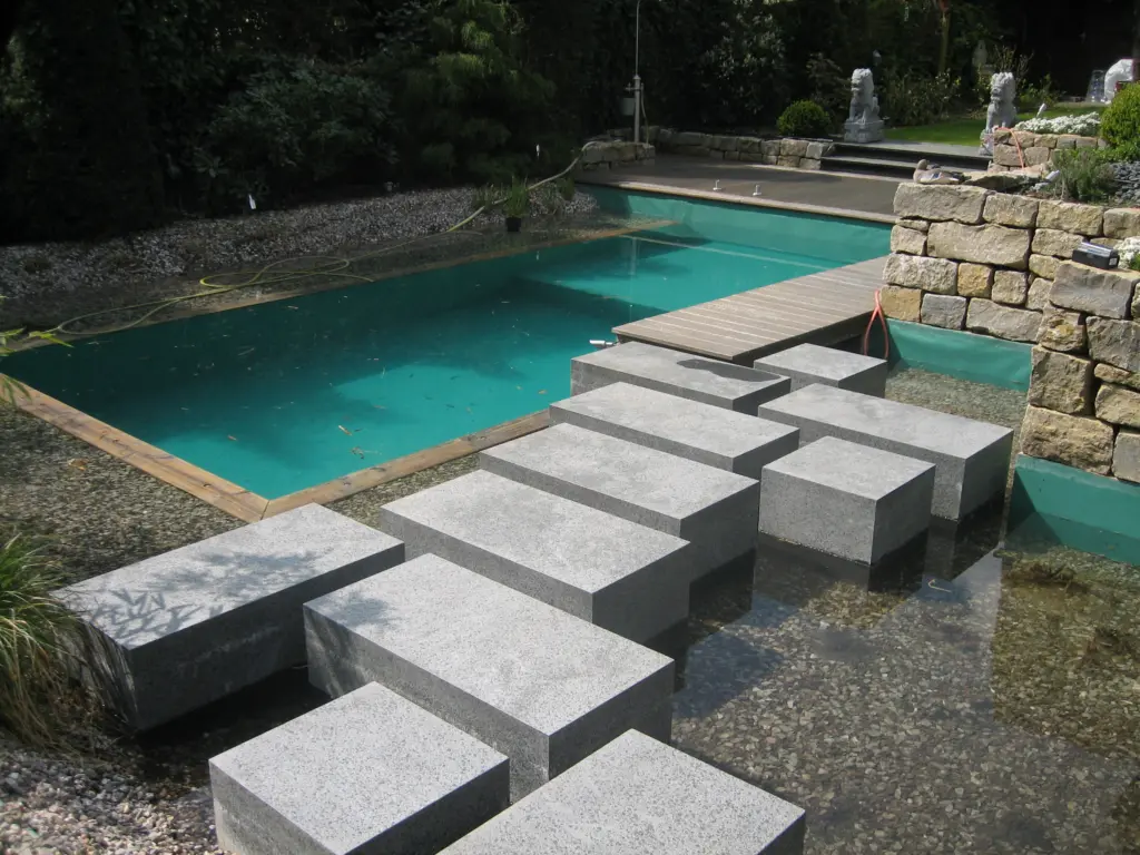 Schwimmteich mit Natursteinmauer und Trittstufen bei Tageslicht