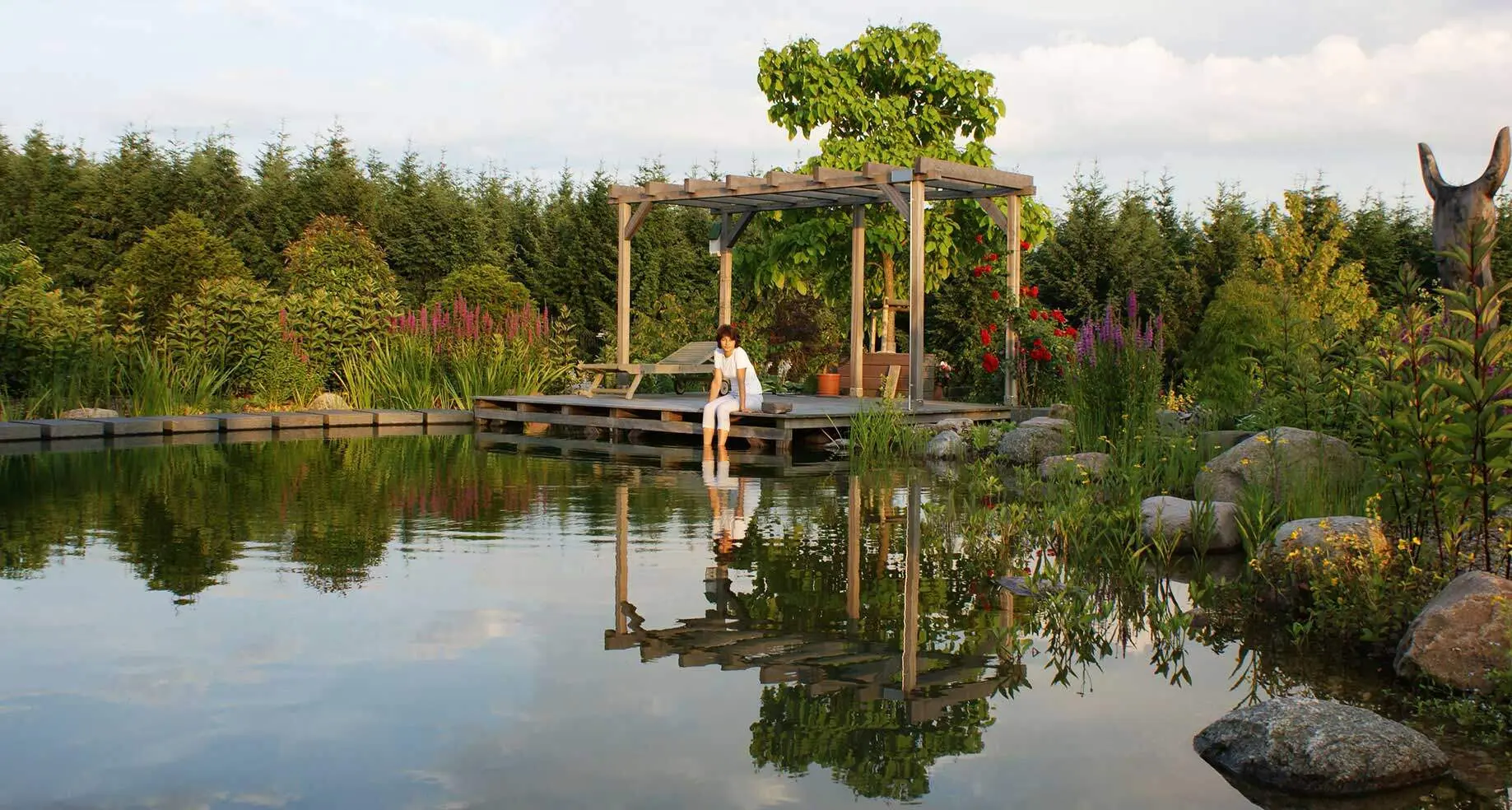 Naturnaher Schwimmteich mit Steg, Pergola und bepflanzter Uferzone